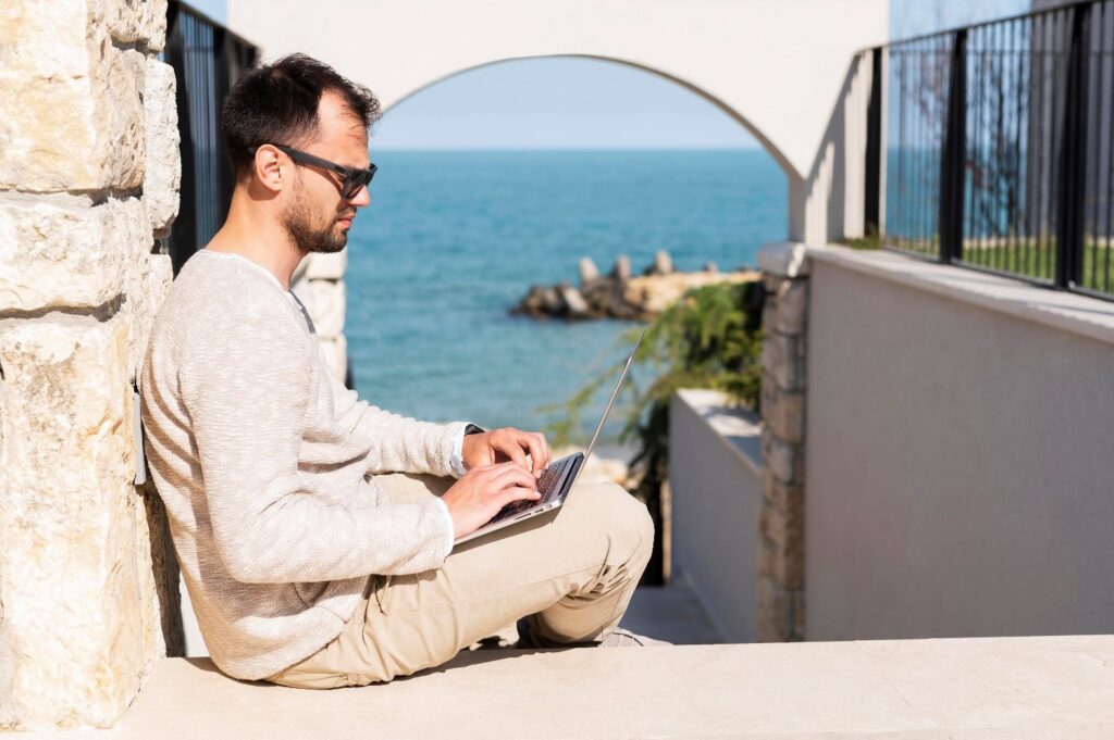 uomo lavora al pc in vacanza con lo sfondo del mare